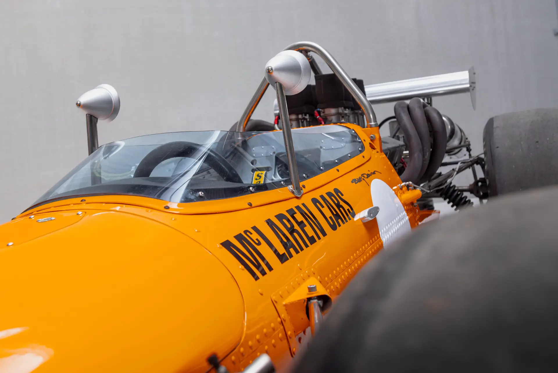 Vue plongeante du cockpit spartiate de la McLaren M10B, montrant le volant trois branches, les compteurs analogiques Smiths, le châssis en aluminium et le levier de vitesses.